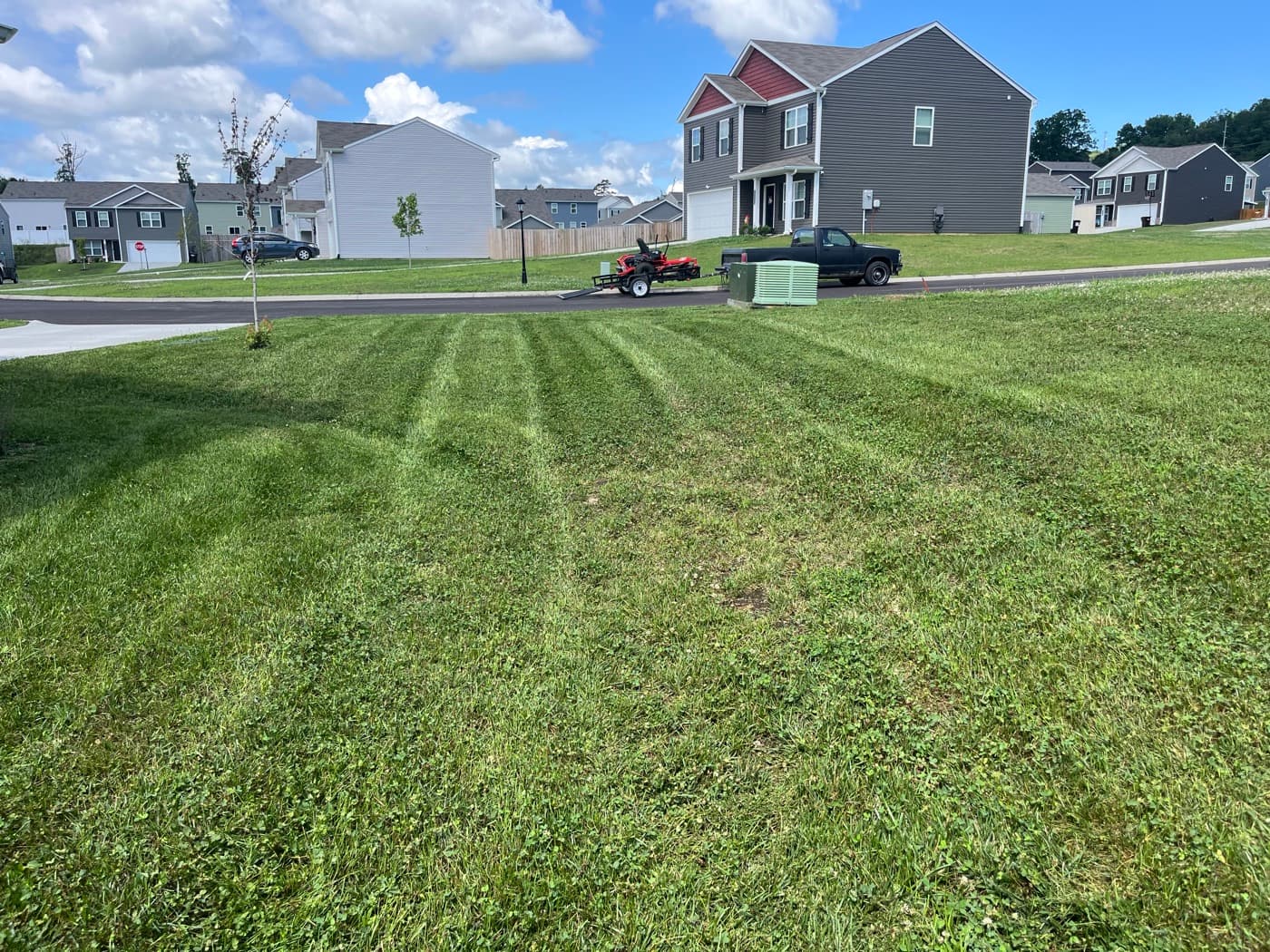 Freshly mowed lawn with clean mow stripes in a Sevier County neighborhood, Roosters mower and trailer at the curb
